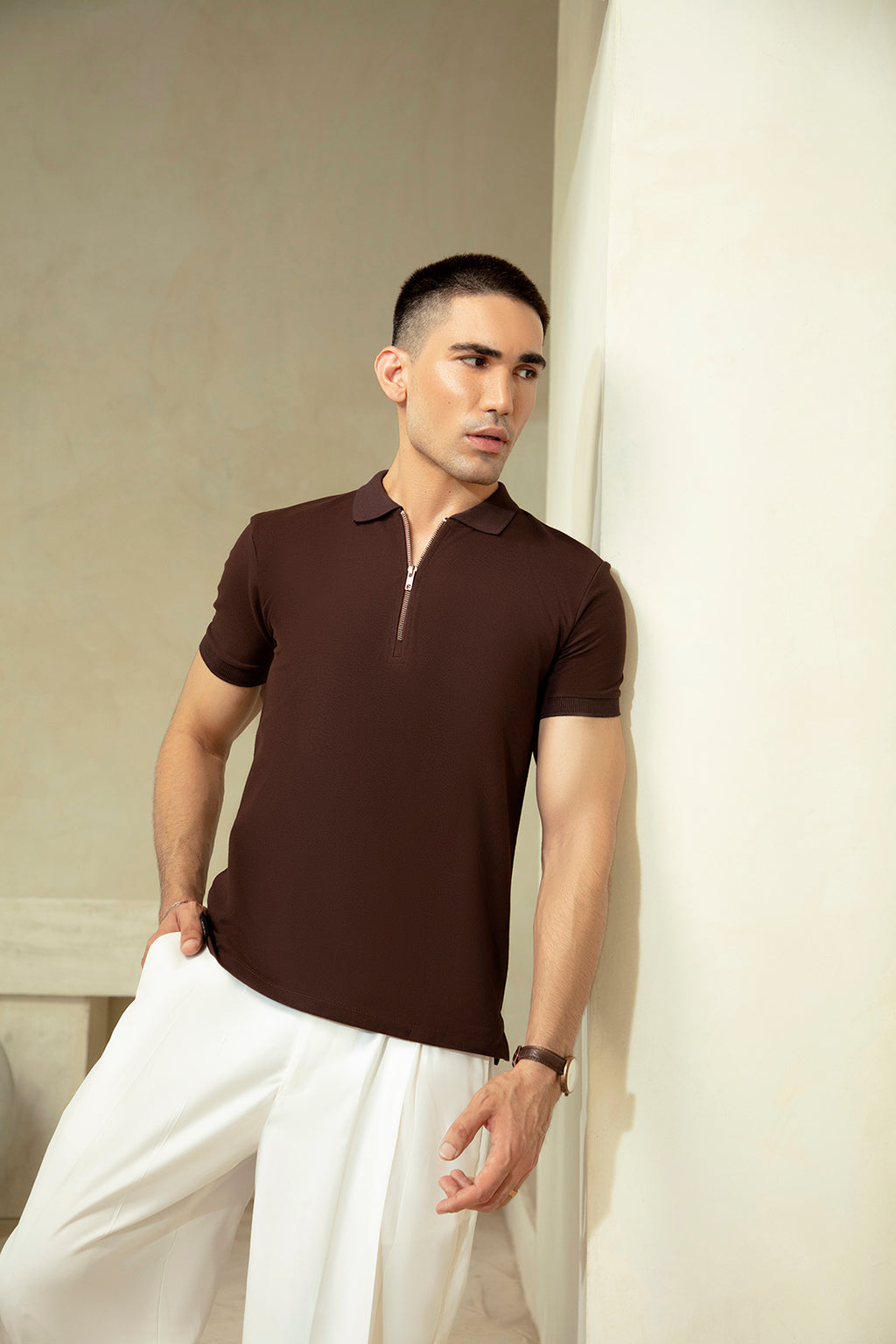 Man wearing a brown polo shirt and white pants against a neutral background