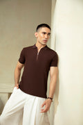 Man wearing a brown polo shirt and white pants against a neutral background