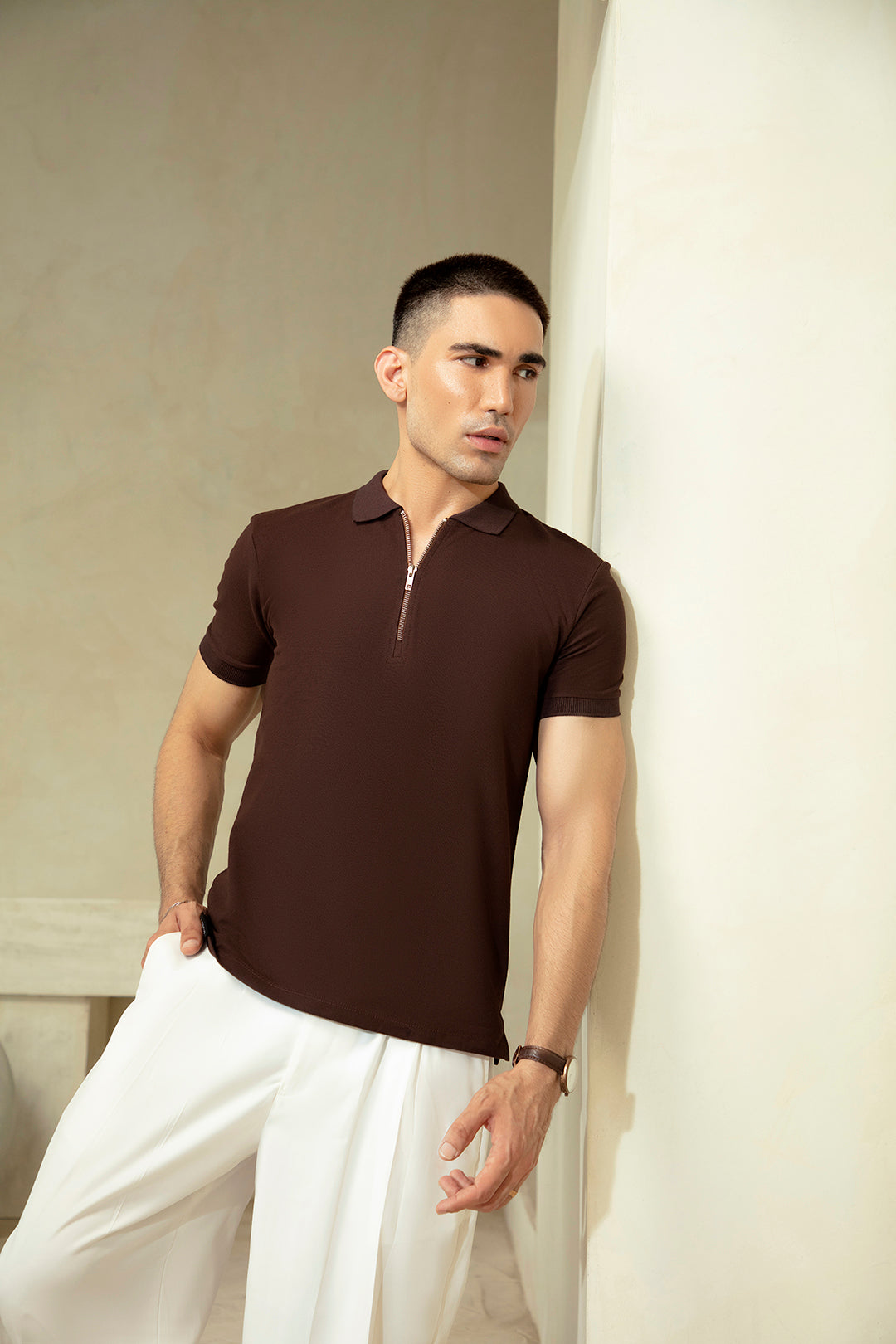 Man wearing a brown polo shirt and white pants against a neutral background