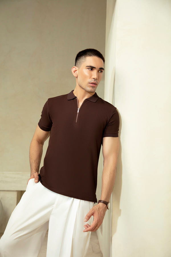 Man wearing a brown polo shirt and white pants against a neutral background